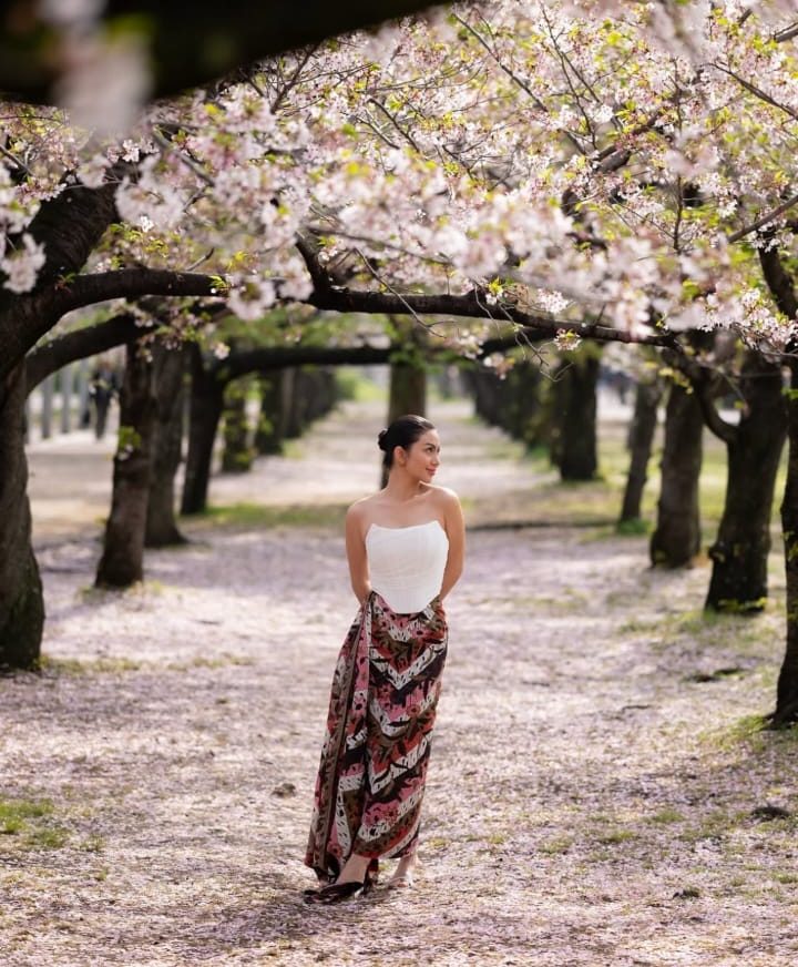 Ariel Tatum mengenakan rok batik saat berfoto dengan bunga sakura. Foto: Dok. Instagram @arieltatum